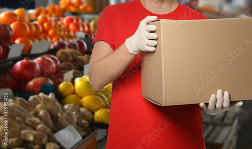 Fototapeta Naklejka Na Ścianę i Meble -  Man with cardboard box against fresh fruits in store, closeup. Wholesale market