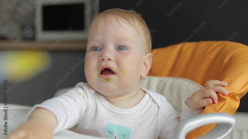 Portrait. Close-up. Cheerful child takes a spoon from his mother and tries to eat. Baby in a feeding chair Portrait. Close-up. Cheerful child takes a spoon from his mother and tries to eat. Baby in a feeding chair