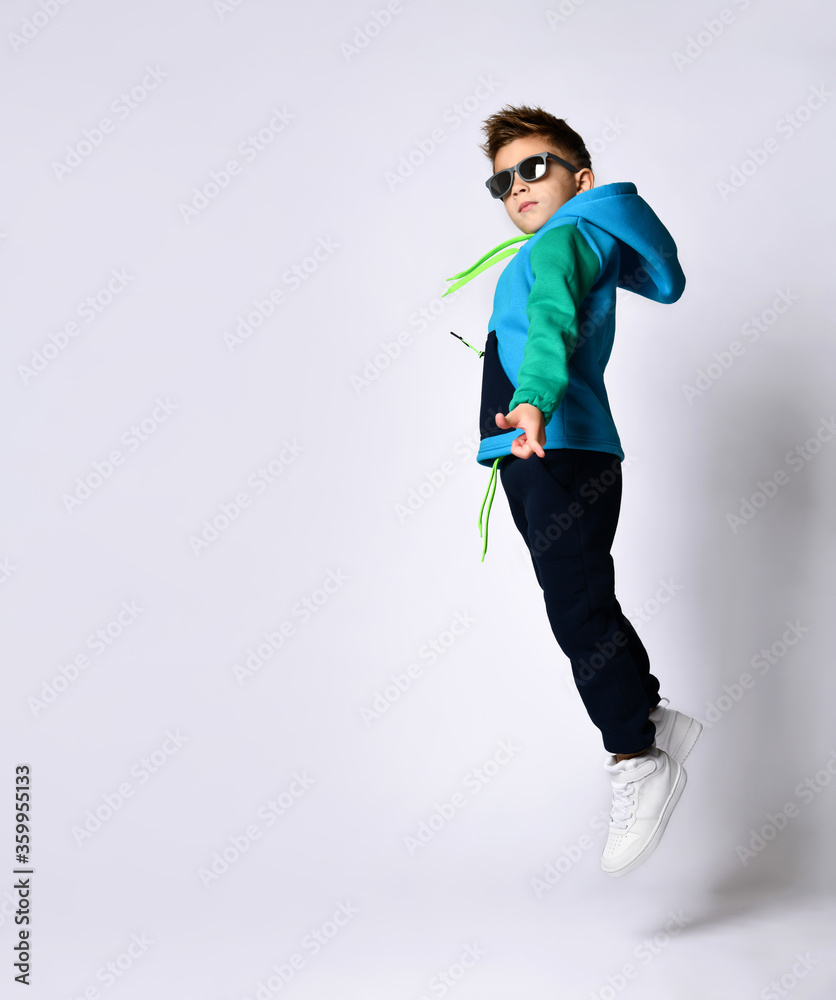 Little kid in sunglasses, colorful sport suit and sneakers. He