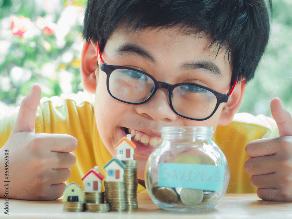 Asian boy holding coins drop a container saving money to save money invest for future and buy home.Concept loan, property ladder, financial, real estate investment and bonus. Asian boy holding coins drop a container saving money to save money invest for future and buy home.Concept loan, property ladder, financial, real estate investment and bonus.