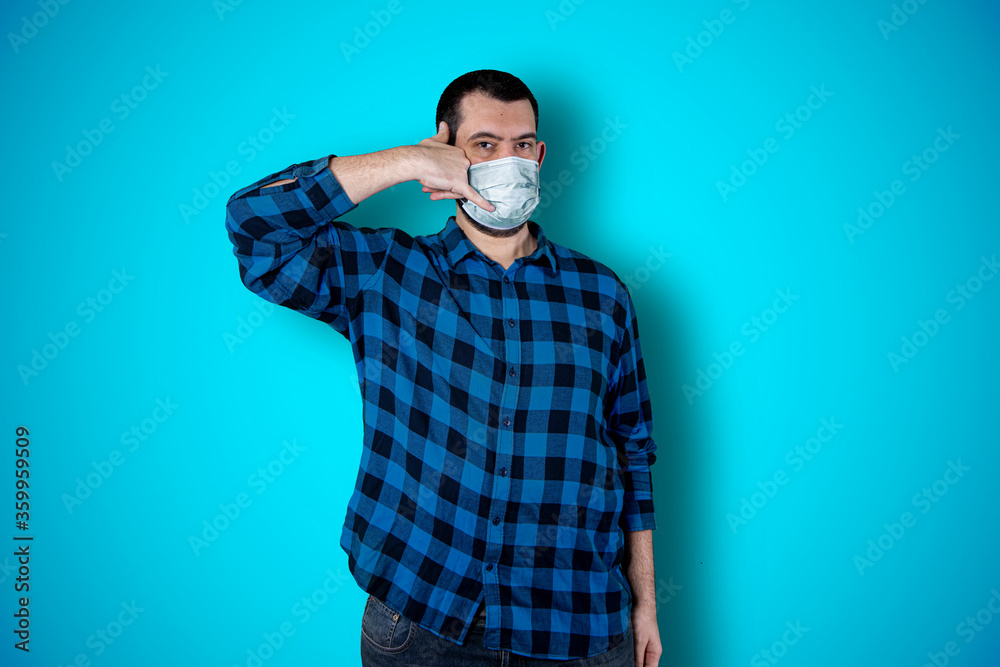 Handsome bearded man using mask and making phone gesture over blue studio background. Coronavirus concept Handsome bearded man using mask and making phone gesture over blue studio background. Coronavirus concept