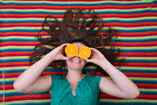 beautiful young girl holding oranges in front of the eyes  with a colorful background