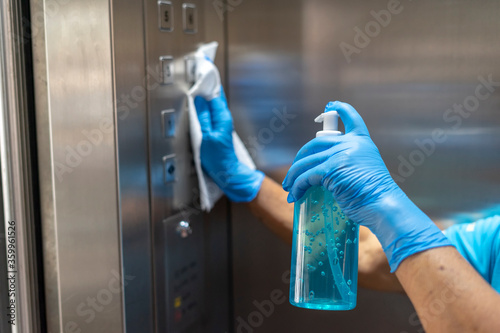 Papier peint Closeup of old staff hand using wet wipe cleaning an elevator push button control panel with a blue sanitizer bottle