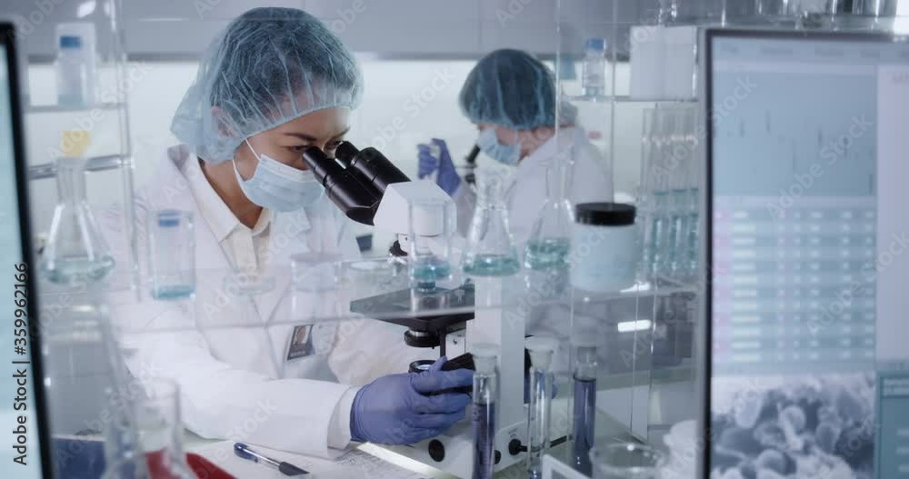 Female team working in modern laboratory. Studying genetic material with microscope. Using computer