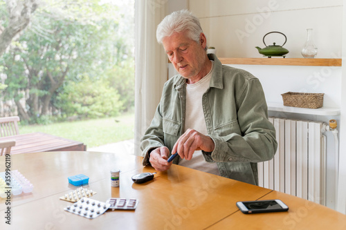 Retired diabetic senior man using glaucometer during blood sugar test while sitting at table