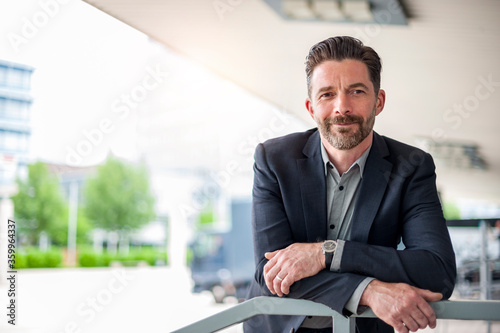 Portrait of confident entrepreneur leaning on railing outside office building in city photo