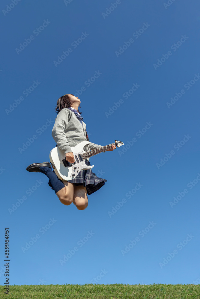 青空を背景にジャンプをしながらエレキギターを演奏する女子高校生 Stock Photo Adobe Stock