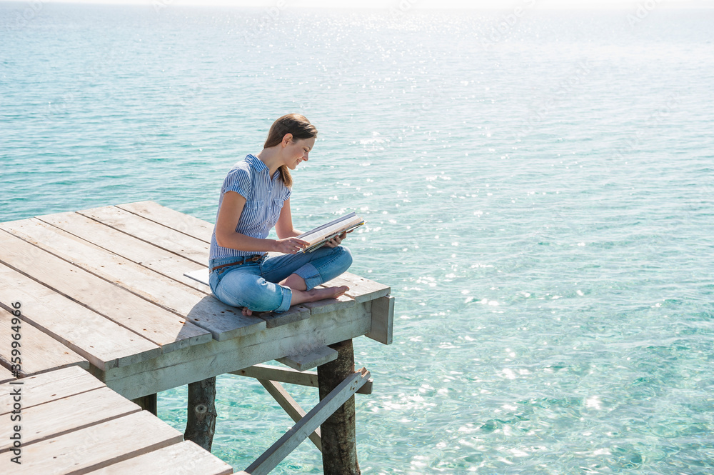 Woman sitting on jetty reading magazine, Mallorca, Spain Woman sitting on jetty reading magazine, Mallorca, Spain