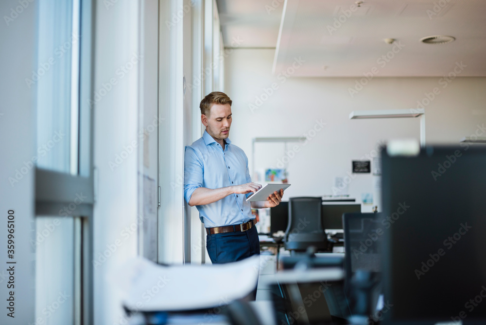 Businessman standing at the window in office using tablet Businessman standing at the window in office using tablet