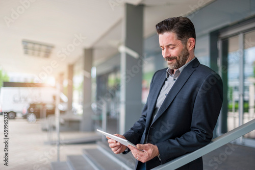 Smiling bearded entrepreneur looking at digital tablet while standing outside office building photo