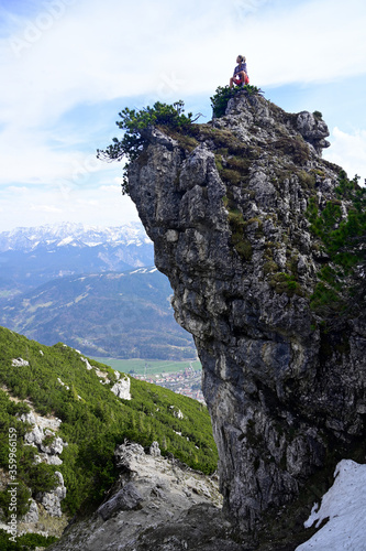 Woman sitting on rocky mountain peak after hiking while looking at landscape against sky photo