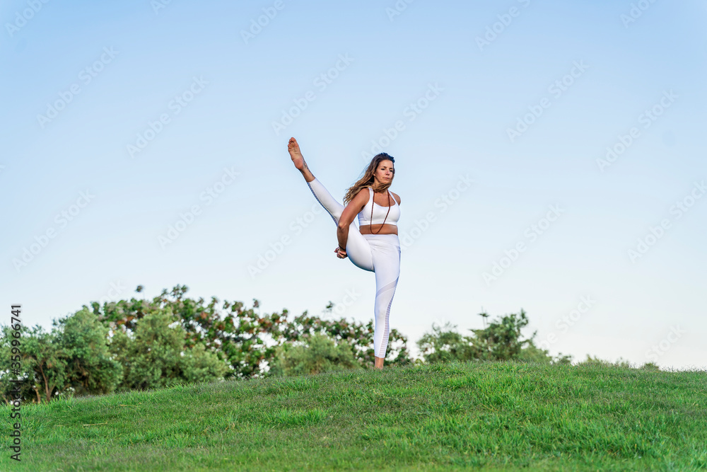 Woman doing yoga on a meadow lifting her leg Woman doing yoga on a meadow lifting her leg