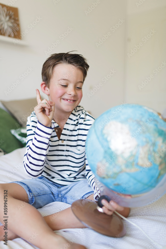Portrait of smiling little boy sitting on bed with his globe Portrait of smiling little boy sitting on bed with his globe