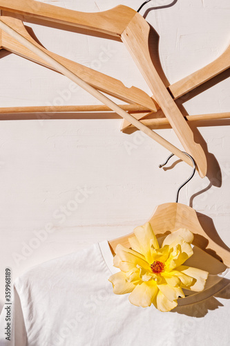 Creative floral background. A white cotton T-shirt is hung on a wooden coat hanger and decorated with a yellow flower. Fashionable layout.