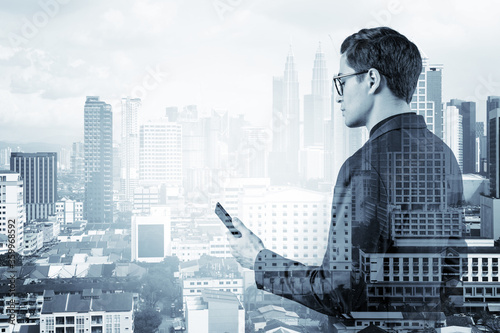 Canvas Print Young handsome businessman in suit and glasses using phone and thinking how to tackle the problem, new career opportunities, MBA