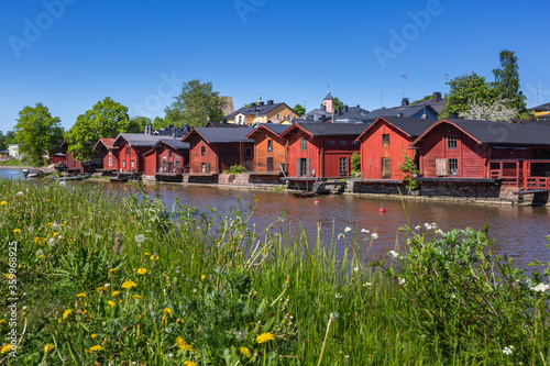 Old red wooden buildings on the river and green grass on foreground, Porvoo, Finland