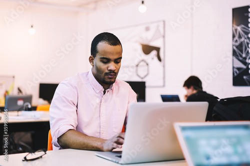 Concentrated skilled male IT programmer developing operative system upgrading old  one with new code working in modern coworking office using laptop computer connected to free wireless internet
