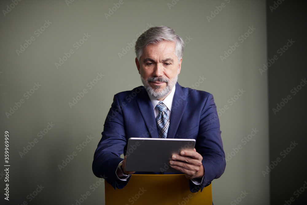 Mature businessman sitting on a chair using tablet Mature businessman sitting on a chair using tablet