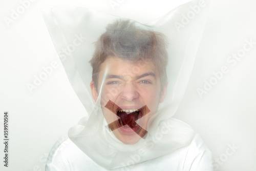 Portrait of screaming teenage boy wearing  transparent mask with cross on his mouth