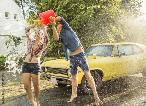 Friends washing yellow vintage car in summer having fun photo