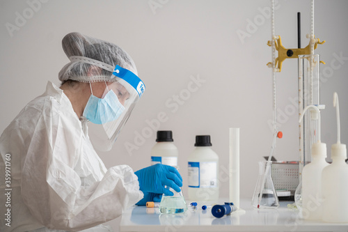 Woman in protective wear sitting at desk researching on epidemiology