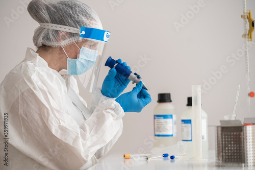 Woman in protective wear sitting at desk researching on epidemiology photo