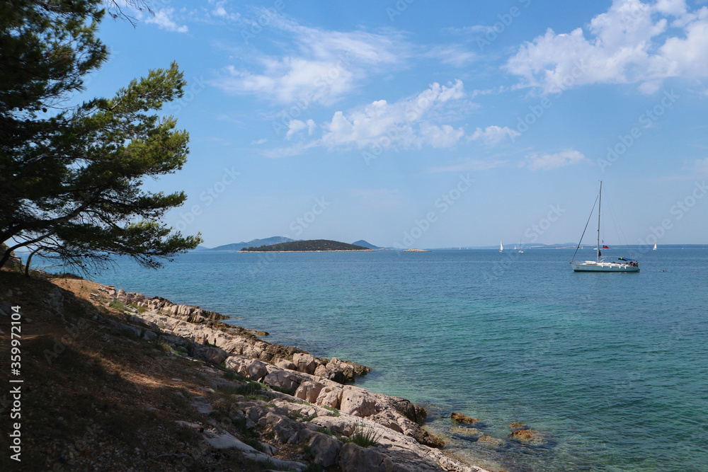 Dalmatian scenery, blue sky and clear turquoise sea with many islands covered by pine forest and boats sailing by