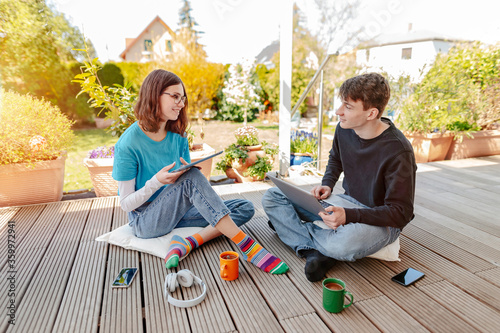 Teenage couple sitting on terrace learning together with laptop and digital tablet