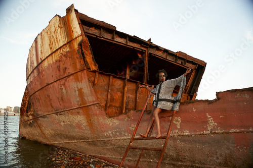 Woman wearing dress and sitting on rusty ship wreck