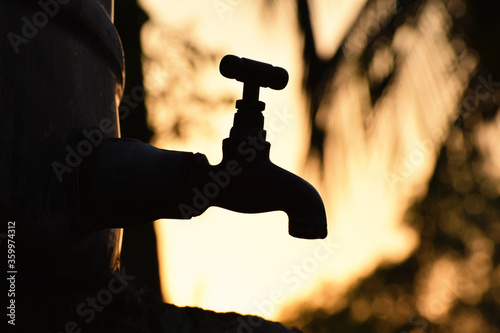 Silhouette of old vintage metal tap alone in outdoor natural environment during golden hour of sunrise, water shortage 