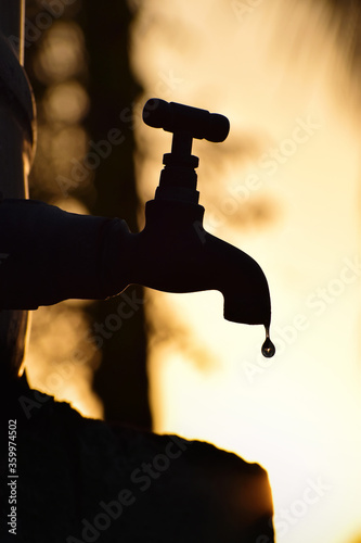 vertical / portrait-oriented, Silhouette of old vintage metal tap leaking water droplet. Alone in outdoor natural environment during golden hour, wallpaper 