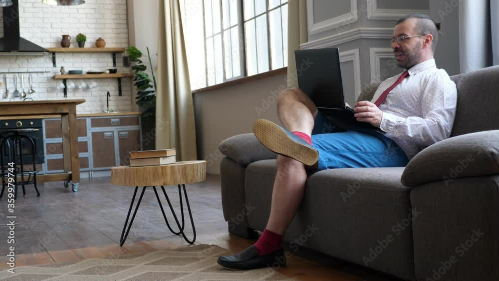Work at home in quarantine. Businessman on the couch chatting in video chat. A man in shorts and a tie. Work at home in quarantine. Businessman on the couch chatting in video chat. A man in shorts and a tie.