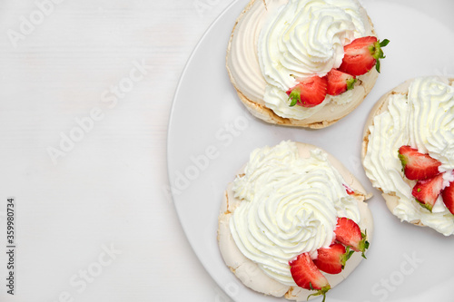 Top view of three Pavlova meringue cakes with fresh strawberry on a white plate on white background with copy space. Homemade pastry.