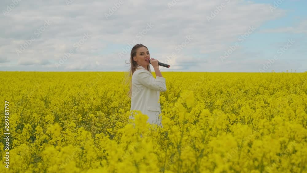 Beautiful girl singer in a yellow field dancing and energizing looking at the camera Beautiful girl singer in a yellow field dancing and energizing looking at the camera