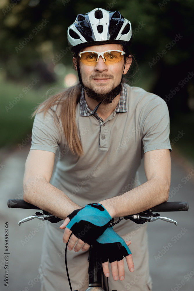 Portrait of man in a yellow sunglasses and helmet standing with bicycle on road and looking into camera. High quality Portrait of man in a yellow sunglasses and helmet standing with bicycle on road and looking into camera. High quality