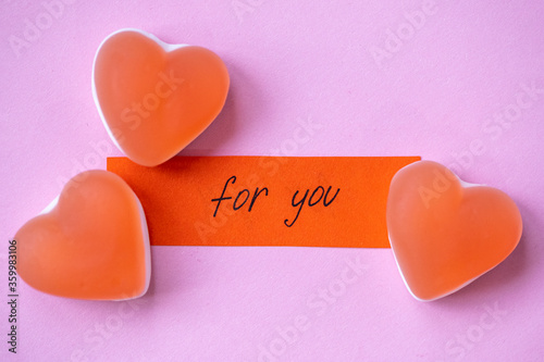 Red candy marmalade in shape of heart with a note FOR YOU on pink background. Sugar gummy candy. Valentine's Day concept. Geometric pattern. Minimal design, flat lay, top view.