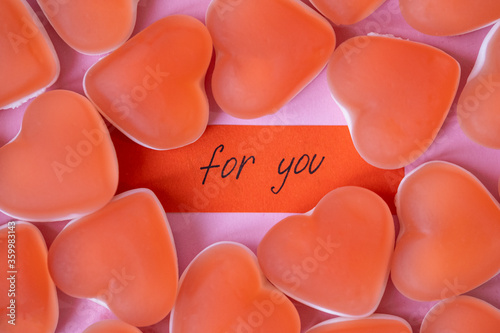 Red candy marmalade in shape of heart with a note FOR YOU on pink background. Sugar gummy candy. Valentine's Day concept. Geometric pattern. Minimal design, flat lay, top view.