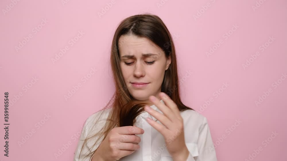 Portrait of unhappy depressed young woman touching damaged hair, worrying about hair loss, sad brunette girl looking at camera, isolated on pink studio background, suffering from hormonal imbalance Portrait of unhappy depressed young woman touching damaged hair, worrying about hair loss, sad brunette girl looking at camera, isolated on pink studio background, suffering from hormonal imbalance