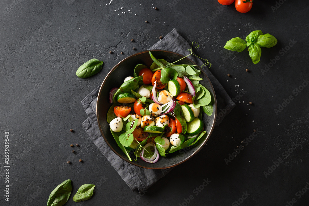 Salad with spinach, cherry tomatoes, onion and Mozzarella on black stone background. Top view.