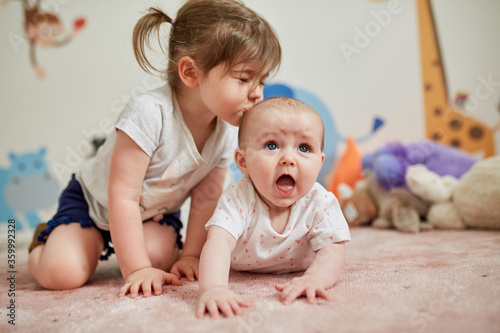 Girl kissing her little sister lying on carpet at home