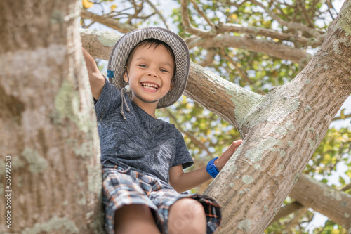 Cute 5 year old mixed race boy wearing a blue hat climbs a tree