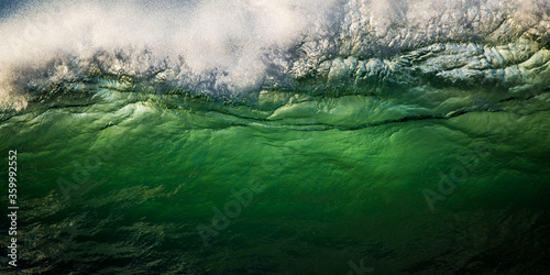 Wave breaking in big surf, green water backlit by sunrise