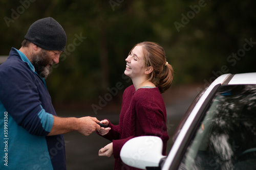 Father handing car keys to teenaged daughter photo