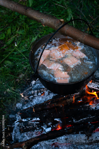 Fish soup boils in cauldron at the stake. Campfire is burning. photo