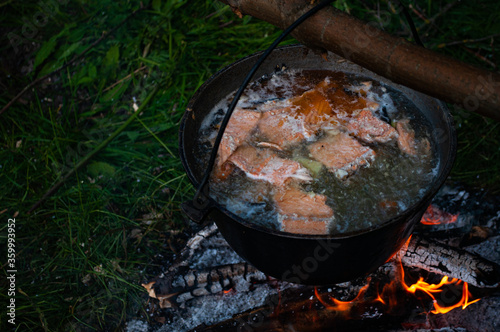 Fish soup boils in cauldron at the stake. Campfire is burning.