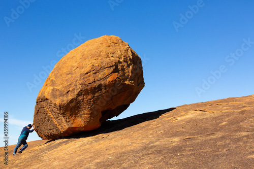 Side view of man trying to push a large granite rock photo