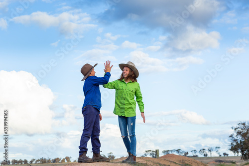 Two country kids high-fiving outdoors against a cloudy sky