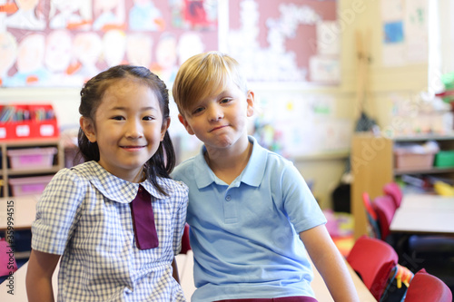 Two school aged children sitting on desk in classroom