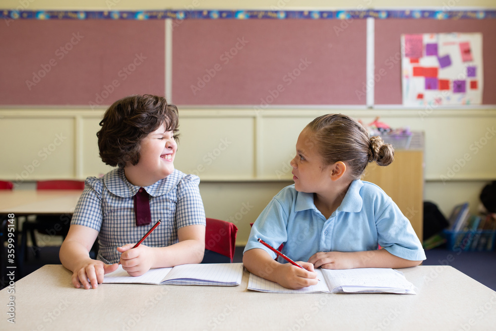Two primary school girl students in a classroom looking at each other Two primary school girl students in a classroom looking at each other