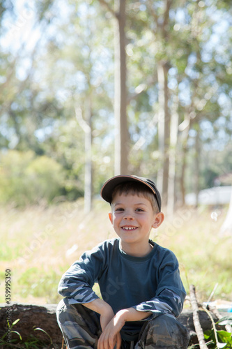 Smiling boy sitting on a log in a paddock by a campfire photo